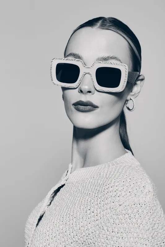 Stylish white woman with pale skin wears large square sunglasses and knitted sweater. Minimalist fashion portrait in monochrome.
