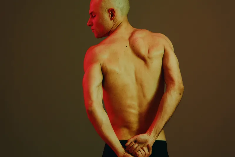Strong man showing his back with crossed arms, highlighted by dramatic lighting in a colorless tone, emphasizing muscle definition and athleticism.