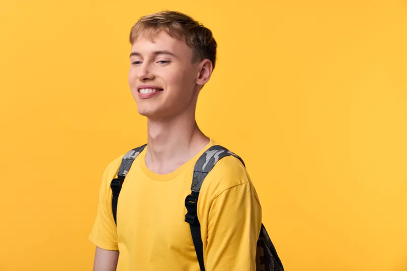 Youthful student in a yellow tee with a backpack, smiling against a bright backdrop, conveying casual energy, everyday style, and optimistic vibe for lifestyle and youth fashion.