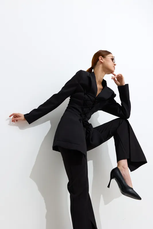 fashion woman in black suit posing confidently against white background, wearing high heels and sunglasses, showcasing contemporary style and sophistication