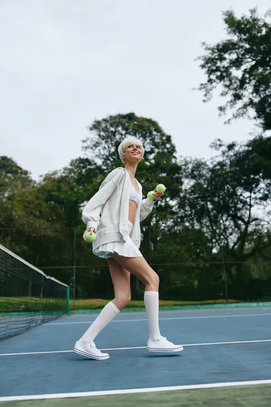 Young woman enjoying a sunny day on the tennis court, wearing a sporty outfit and smiling, surrounded by lush greenery and a bright atmosphere