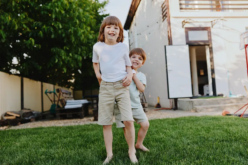 Happy children playing together on a sunny day in the garden, enjoying their time outdoors with laughter and smiles, surrounded by green grass and trees.