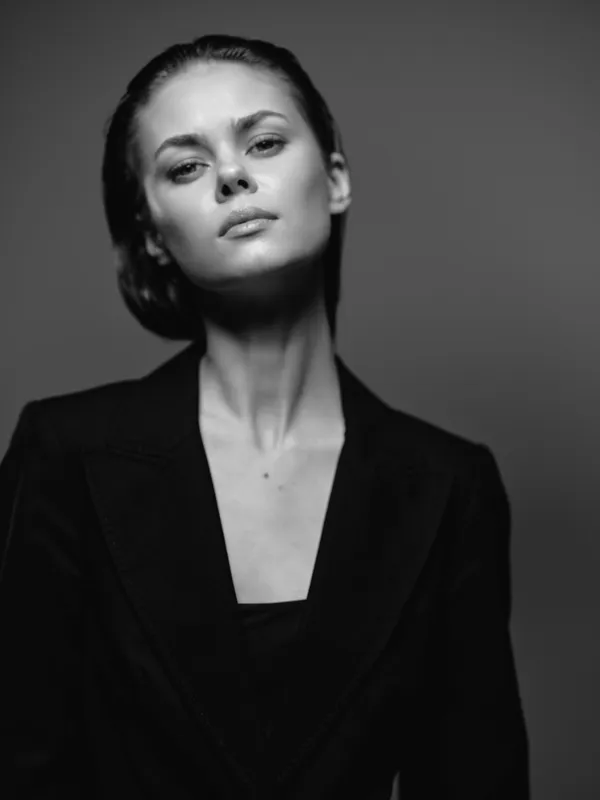 Black and white portrait of a serious woman in a dark blazer with natural makeup and slicked-back hair.