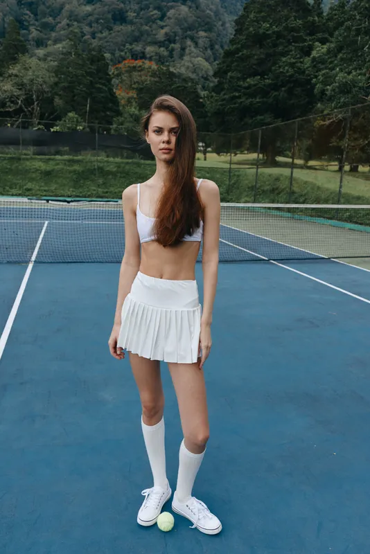 Young athletic woman in sporty white outfit on a tennis court, exuding confidence and determination, showcasing a healthy lifestyle and joy of sport