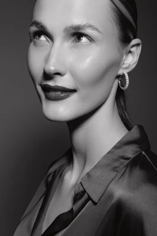 Close-up portrait of a fair skinned Caucasian woman with slicked back hair and hoop earrings in monochrome. Elegant confident mood with soft studio lighting and smooth skin texture.