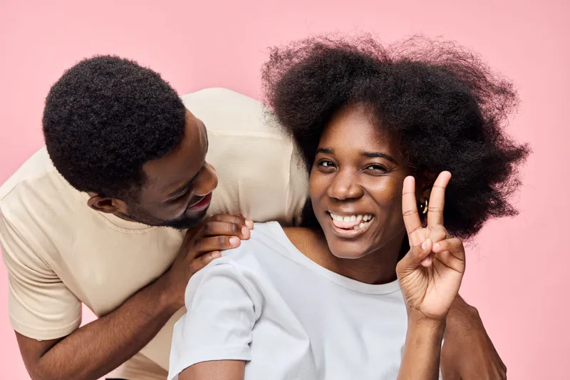 Happy couple with natural textured hair posing together on a pink background, showcasing vibrant emotions and friendship