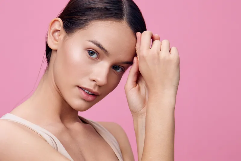 Portrait of a young woman with light makeup against a pink background, showcasing natural beauty and soft emotions, ideal for beauty and fashion concepts