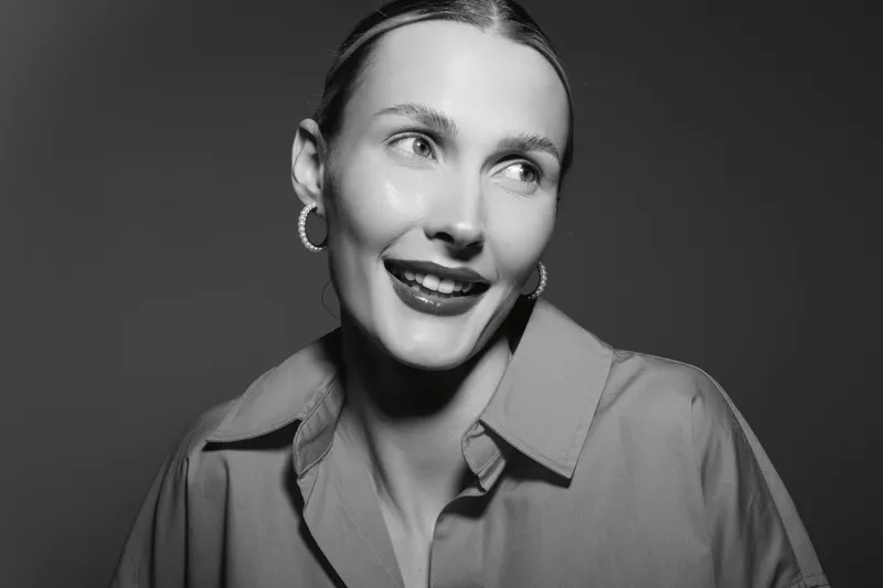 Portrait of a smiling young white woman with light skin and blonde hair, wearing hoop earrings and a shirt, looking away. Concept of joy, beauty, and fashion in studio lighting.