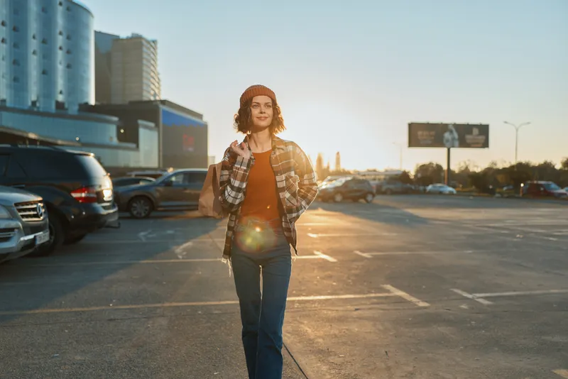 Woman walking in an urban parking lot at sunset, a candid moment with authenticity and mindful living vibe, golden hour glow and emotional storytelling in a modern casual portrait.