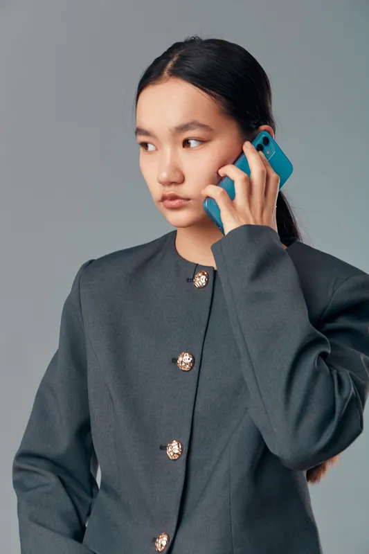 Young woman in gray jacket talking on mobile phone looking aside with serious expression on neutral background for communication or business technology concept.