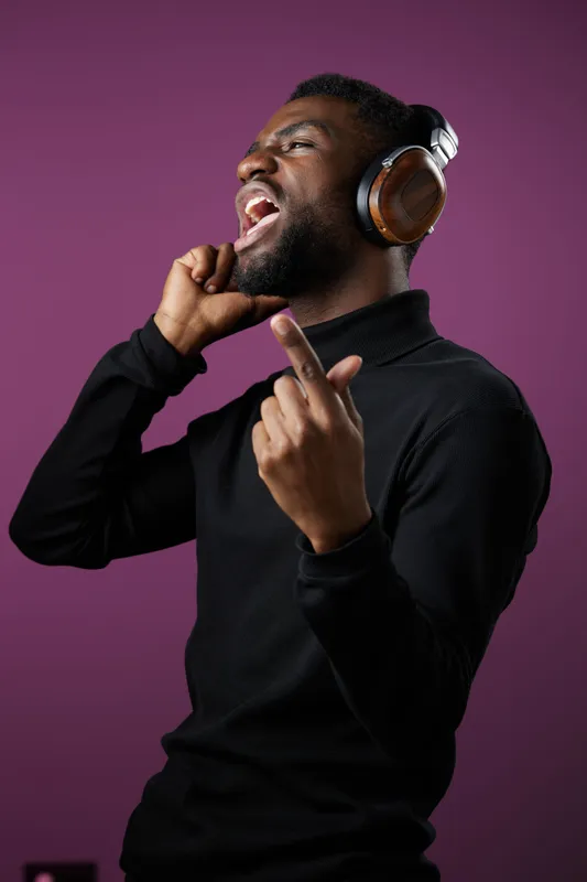 Energetic young man singing passionately while wearing headphones, showcasing joy and love for music against a vibrant purple background
