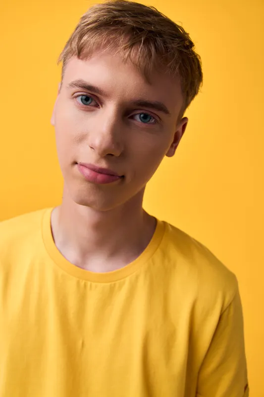 Closeup of a young man in a yellow shirt against a bright yellow background, showcasing a calm smile and casual style, perfect for lifestyle, fashion, and positive mood imagery in advertising,