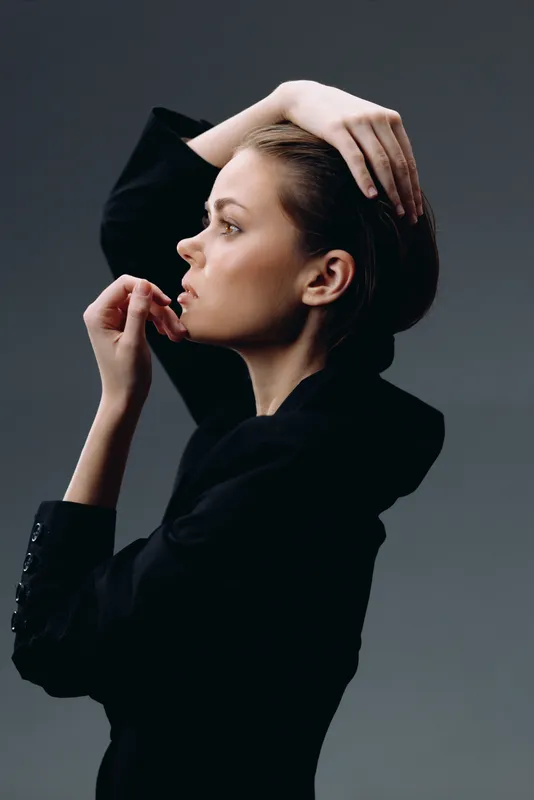 Profile of a thoughtful woman in black clothing against a dark background, showcasing elegance and calm emotion.
