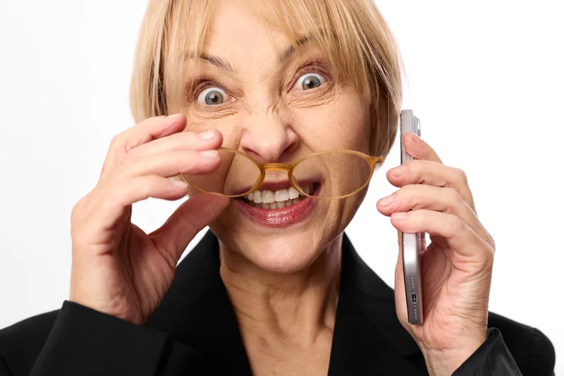 Fear and shock on a blonde woman as she panics with a phone near her ear, using a paper megaphone for whisper communication, studio portrait showing anxiety and stress.