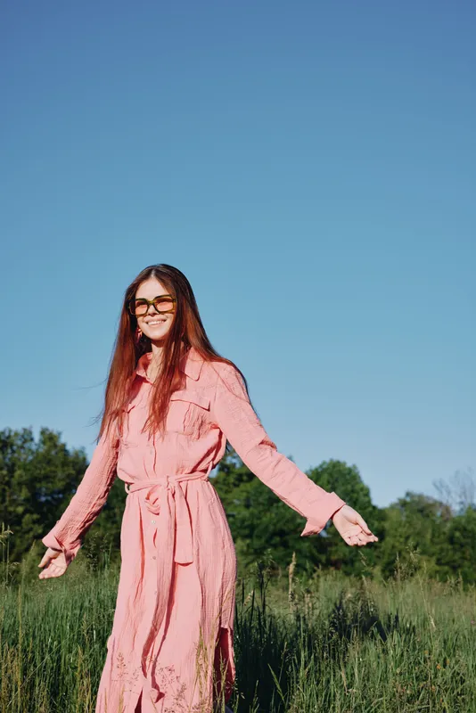 Young woman in a pink dress enjoying a sunny day in a green field, radiating happiness and joy, perfect for seasonal lifestyle concepts