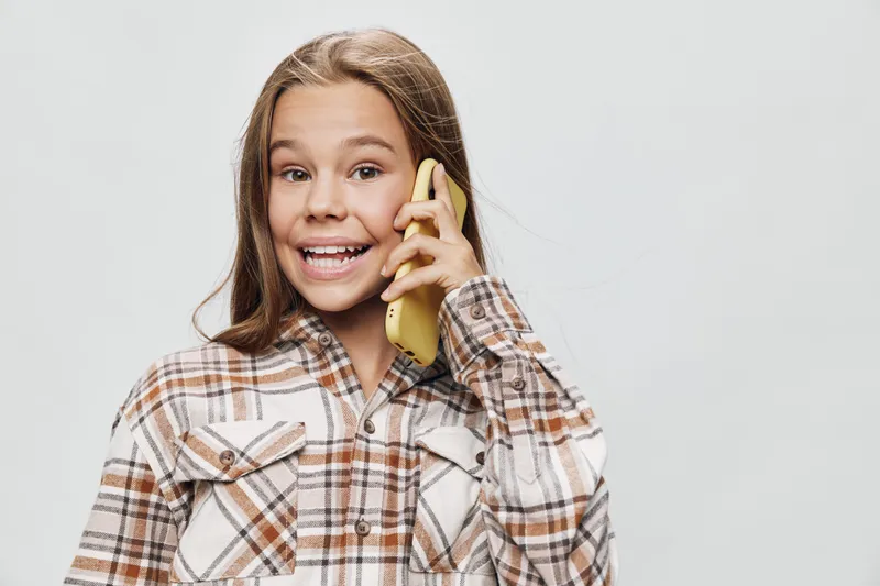 Girl talking on phone smiling wearing plaid shirt in studio with light background, communication and technology concept for lifestyle and casual youth portrait.