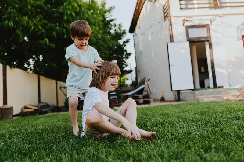 Happy boys playing outdoors, enjoying a sunny day in a backyard, with bright green grass and a playful atmosphere filled with laughter.