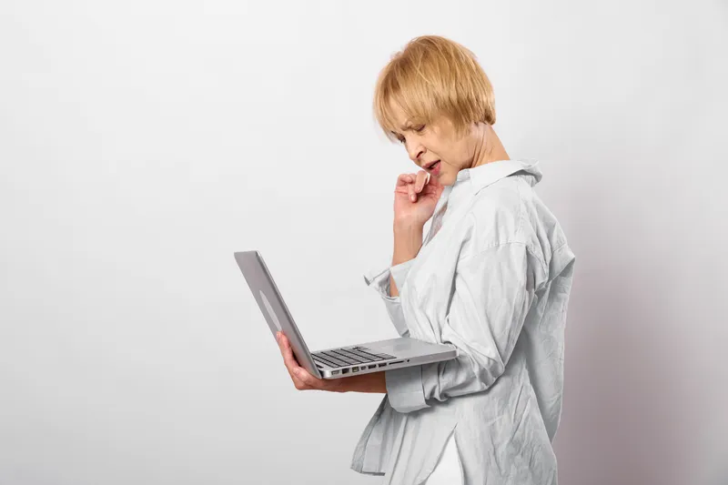 Blonde woman in office, holding laptop, showing headache and stress, hand near face, tired worried expression, isolated on white background, modern work