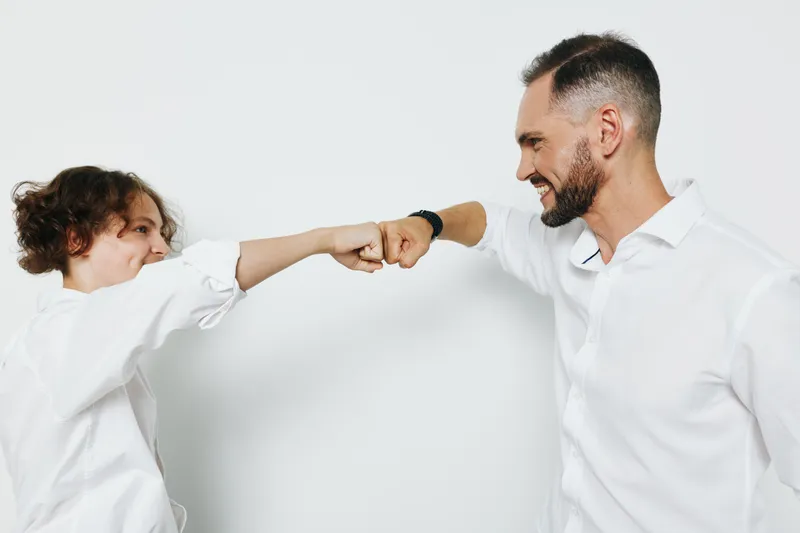 A professional businessman shares a confident fist bump with a colleague against an isolated colored background, signaling teamwork, ambition, and strong emotional energy in a corporate setting.