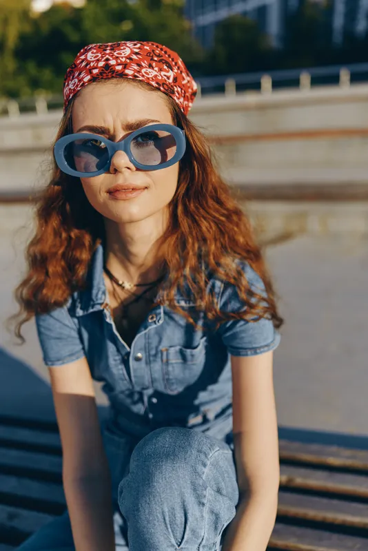 lifestyle woman in modern boho-western denim street style wearing oversized blue sunglasses and red bandana captured in vibrant film color lighting outdoors