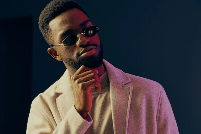 Stylish young man in sunglasses and a light coat against a dark background, exuding confidence and sophistication, ideal for fashion and lifestyle concepts