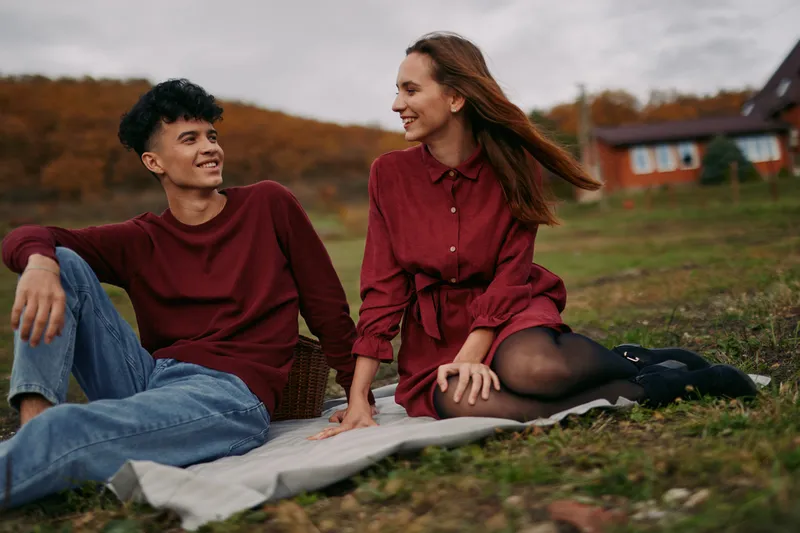 A candid portrait of a young couple sharing a genuine moment outdoors on a picnic blanket, authenticity shown through relaxed body language, warm smiles and natural eye contact conveying trust and