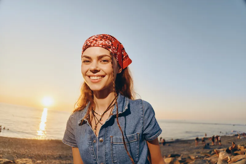 Lifestyle woman in modern boho-western denim street style smiling outdoors with warm sunset film color tones and relaxed beach background.