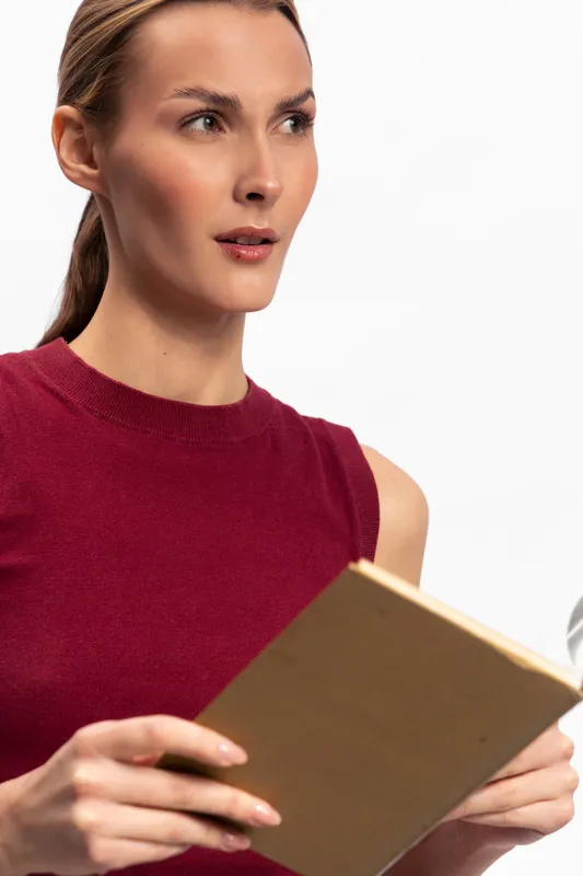 Young woman in sleeveless red top holds notebook and looks thoughtfully to the side. Concept of contemplation, planning, and focused attention in casual setting.