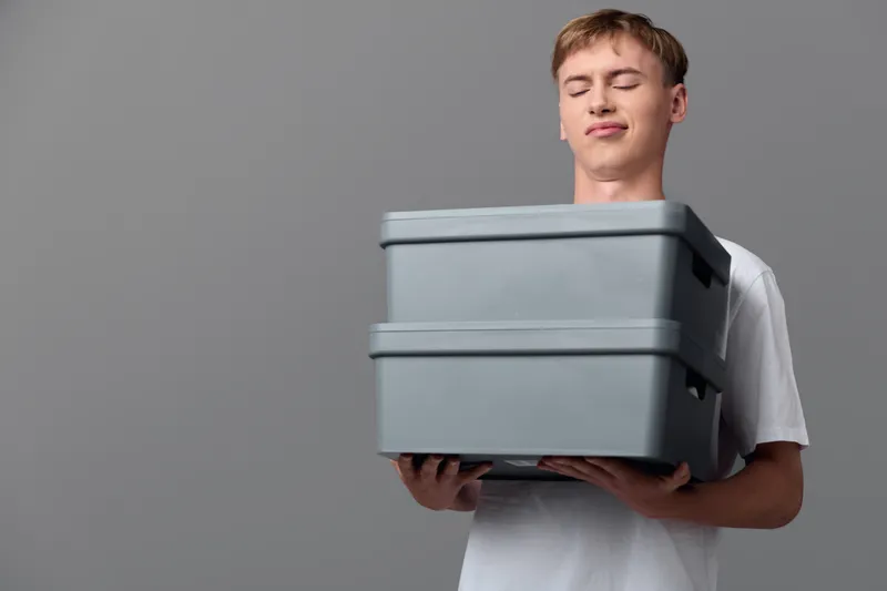 Man holding stacked grey boxes for delivery and storage, illustrating packaging, logistics and inventory in a clean studio setup with focus on workflow and order fulfillment