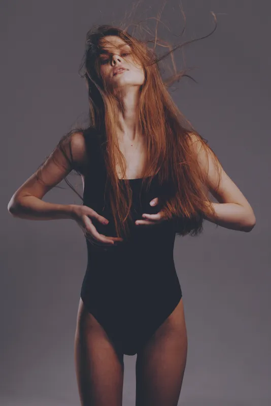 young woman with long hair posing in black bodysuit in moody lighting