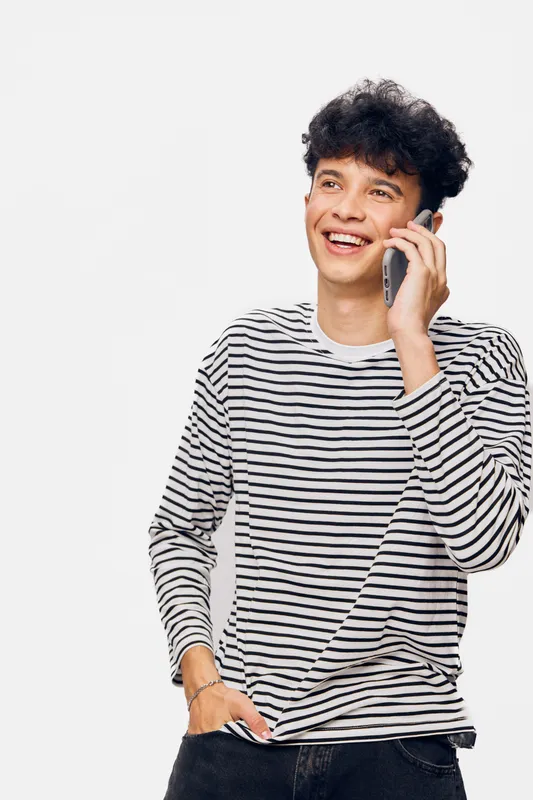 young man talking on smartphone smiling, casual striped shirt, curly hair, joyful expression, white background, communication concept