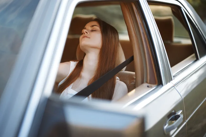 Young woman relaxing in a car, enjoying the breeze with her eyes closed, conveying a sense of calm and peace in a natural setting.