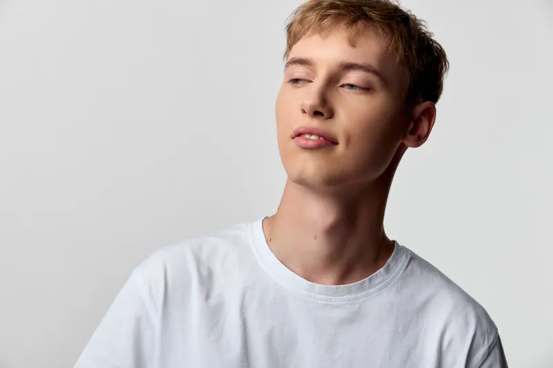 Male model, relaxed expression, white tshirt, looking away, studio shot, casual style, youth vibe, fashion mood, clean background, natural lighting