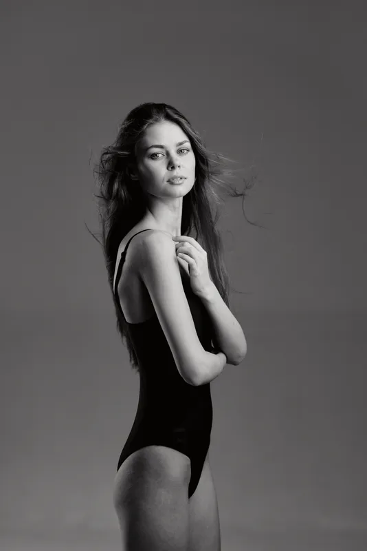 Black and white portrait of a young woman in a swimsuit with a contemplative expression and soft lighting.