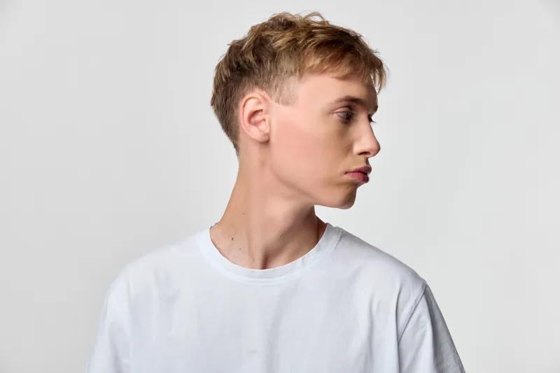 Profile, man, side view, white shirt, studio lighting, minimal fashion vibe with clean lines and soft shadows, studio setting highlighting contemporary style and calm expression.