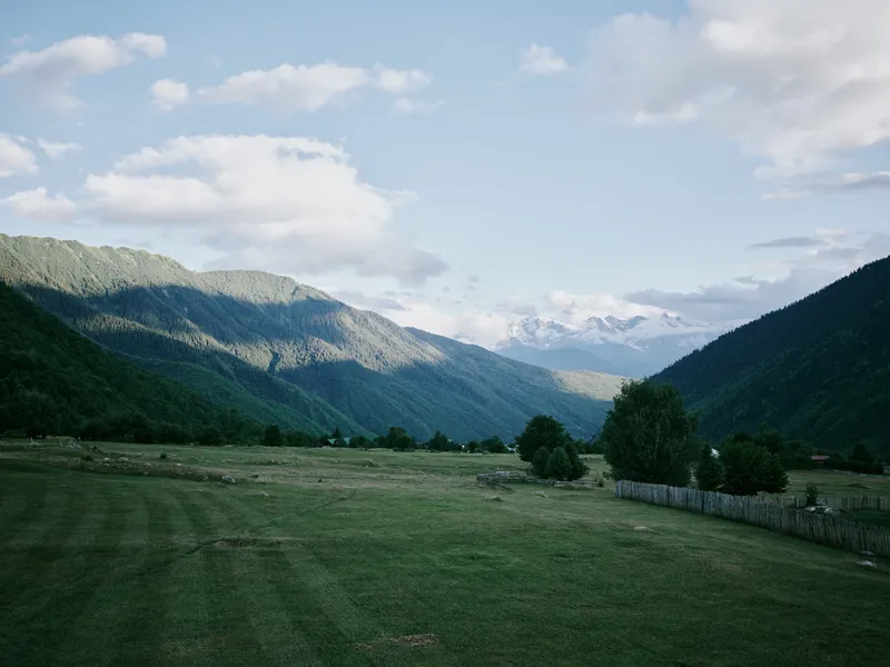 Landscape of a green valley with rolling fields and distant mountains under a clear blue sky, trees along a stone wall, a tranquil rural scene ideal for nature and outdoor stock