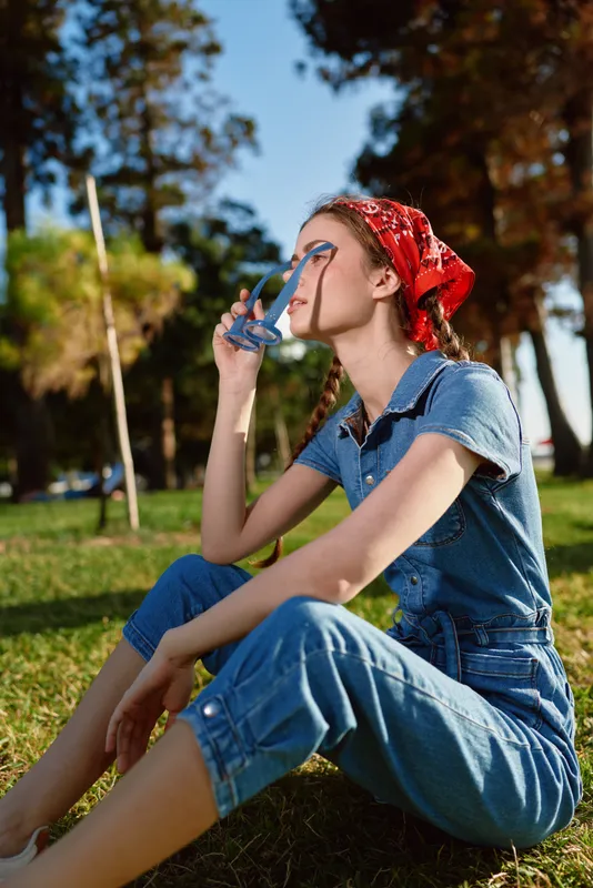 lifestyle woman wearing denim outfit and red bandana enjoys sunny day outdoors in modern boho-western street style with film color mood and natural background
