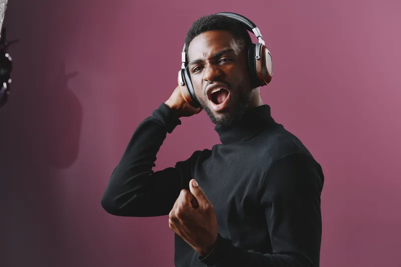 Young Black man enjoying music with headphones, expressing joy and energy against a vibrant purple background