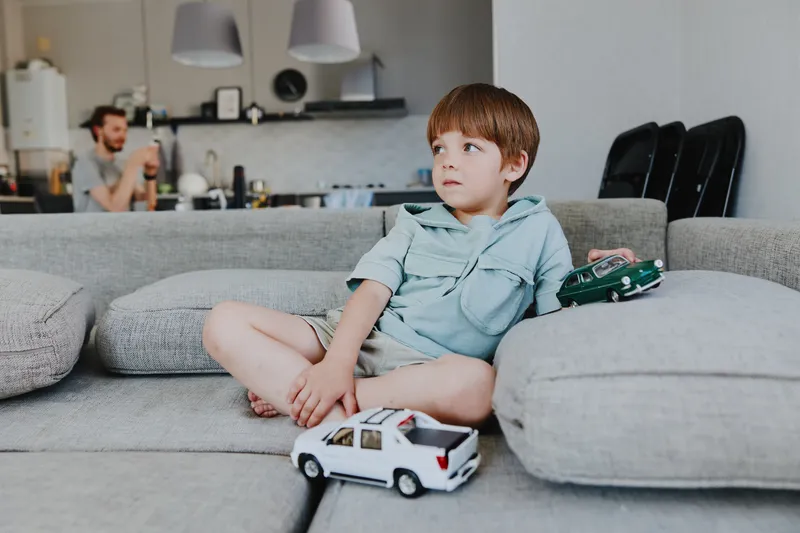 Thoughtful boy playing with toy cars in a cozy living room, showcasing creativity and nostalgia with a warm family atmosphere.