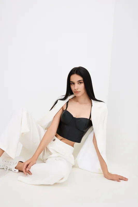 young woman posing sitting against white background wearing a black corset and white loose trousers with a relaxed and stylish mood