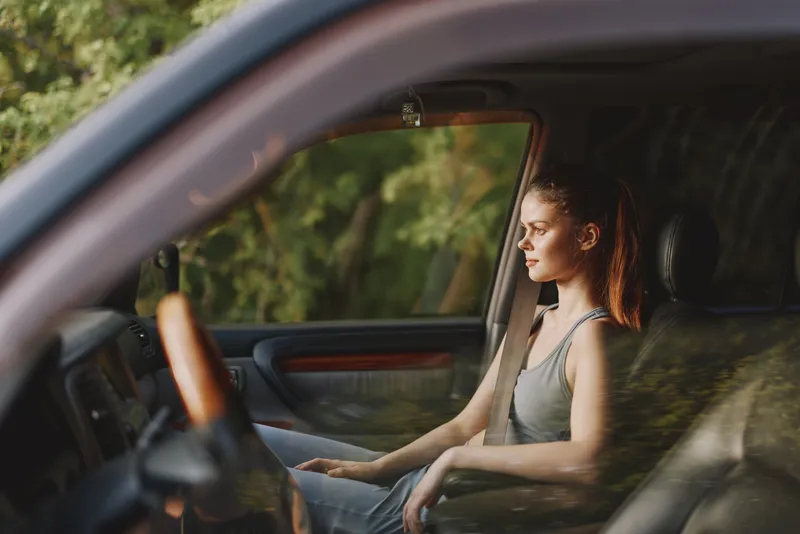 Young woman in a relaxed pose, sitting in a car, enjoying the serenity of nature with a contemplative expression and natural light illuminating the scene