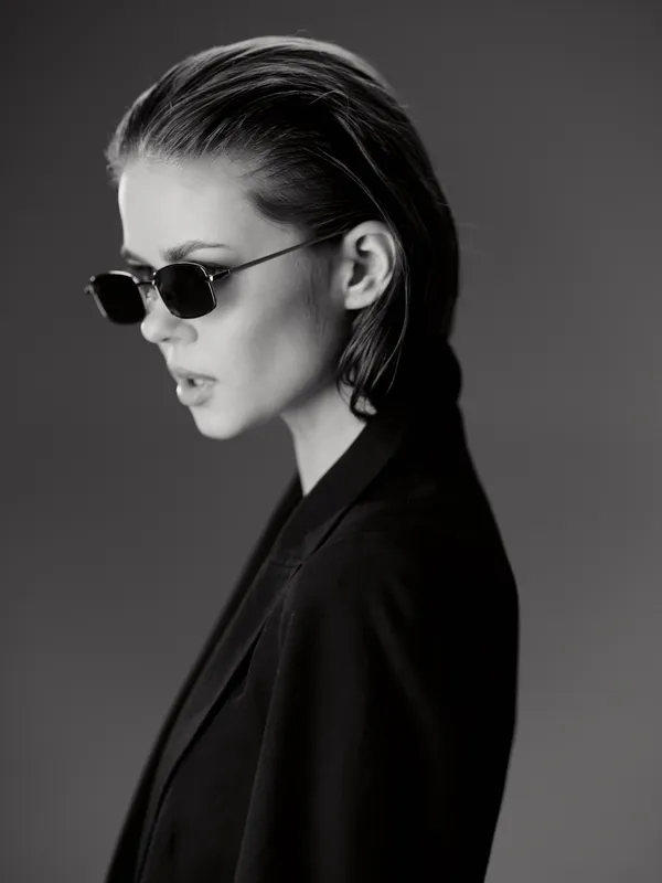 black and white portrait of stylish woman wearing sunglasses and blazer with serious expression in studio lighting