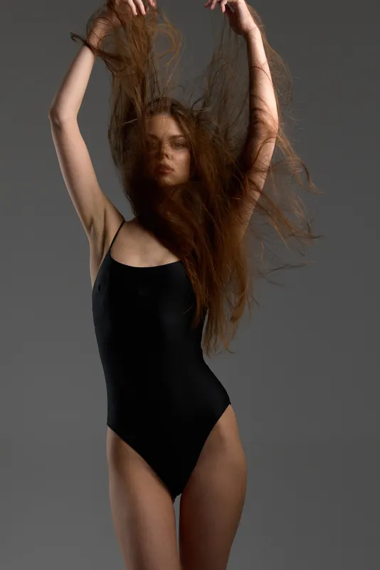 woman in black bodysuit with flowing hair posing confidently against gray background