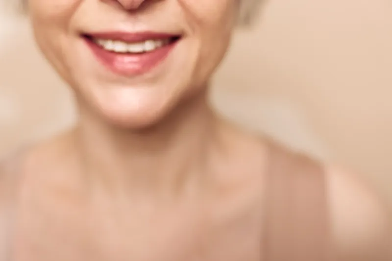 Close-up of middle aged woman smiling with natural skin and soft light on beige background. Concept of happiness, wellness, positive emotion, beauty, and senior lifestyle.