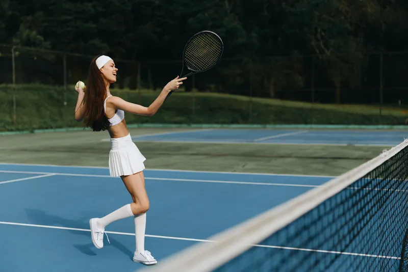 Young female tennis player in sporty outfit joyfully hitting a tennis ball on a vibrant blue court, showcasing her athleticism and energy during the game