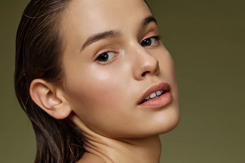 Portrait of a young woman with natural makeup and wet hair, featuring a calm expression and earthy green background, ideal for beauty and wellness concepts