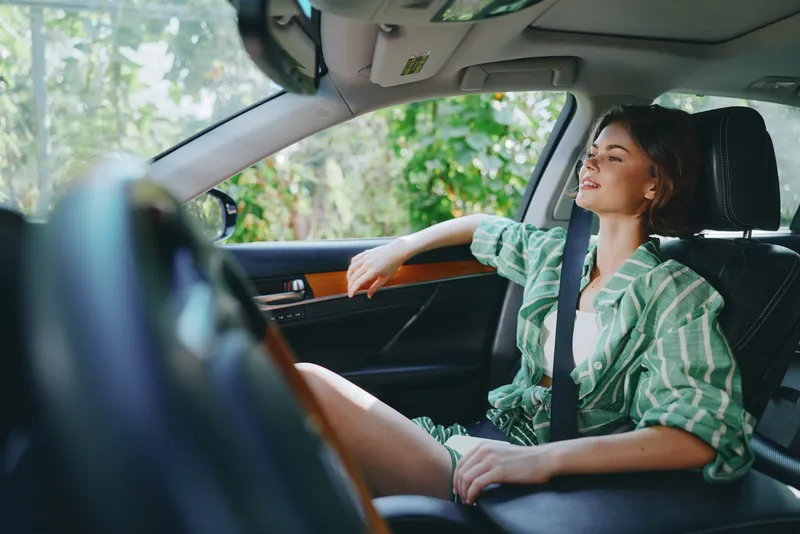 Relaxed woman sits in a modern car interior, hands resting on the armrest, enjoying a calm, comfortable drive.
