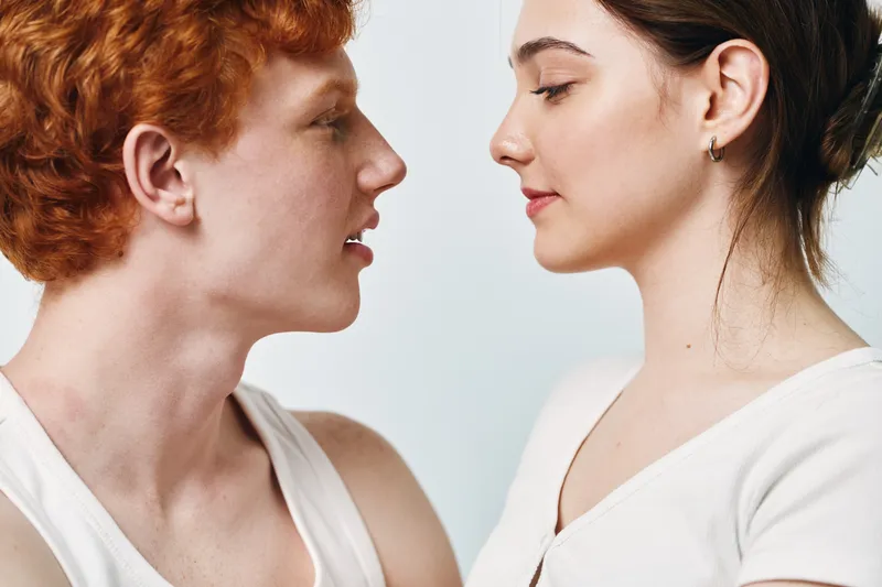 Portrait of redhead man and woman facing each other with closed eyes in minimal studio background. Intimate moment between young couple with calm expressions and natural light.