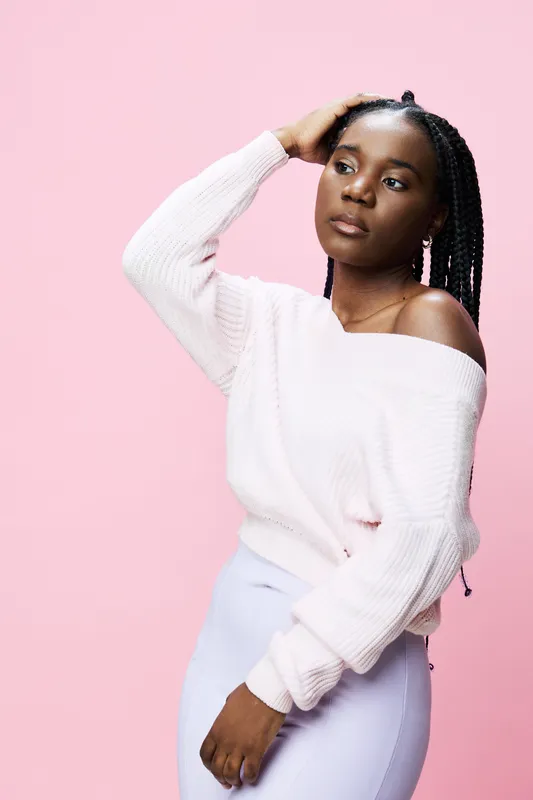 Young African woman in pastel sweater and skirt poses gracefully against a pink background, conveying confidence and style