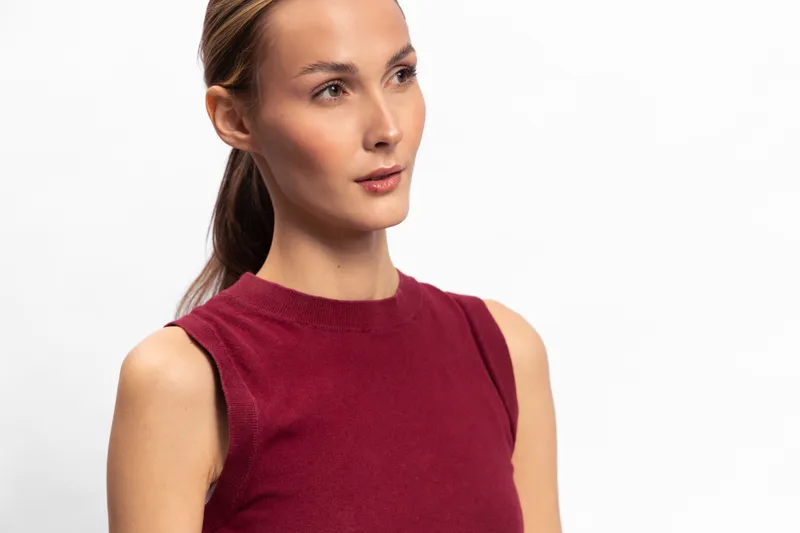Young woman with tied back hair wearing sleeveless red top looks thoughtfully to the side on white background. Concept of contemplation, casual style, and natural beauty portrait.